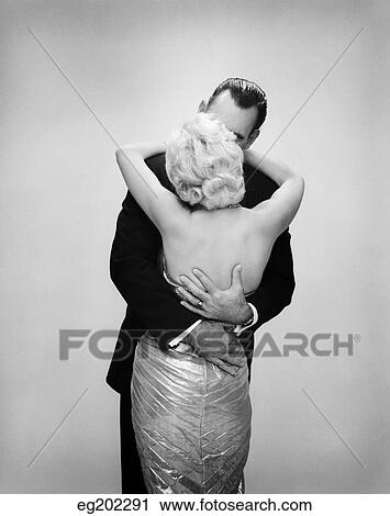 1950S 1960S Kissing Couple Blond Woman Backless Satin Evening Dress Man Embracing From Behind View Large Photo Image Stock Image - 1950S 1960S Kissing Couple Blond Woman Backless Satin Evening Dress Man Embracing From Behind. Fotosearch