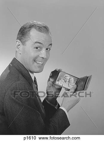 Stock Image - 1950S 1960S Man Smiling Holding Wallet Showing Photo Of Family Looking At Camera. Fotosearch