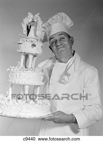 Stock Image - 1950S 1960S Older Man Chef Looking At Camera Smiling Holding 3-Tier Wedding Cake. Fotosearch