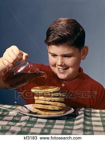 Stock Image - 1950S 1960S Smiling Boy Pouring Syrup On Breakfast Pancakes . Fotosearch