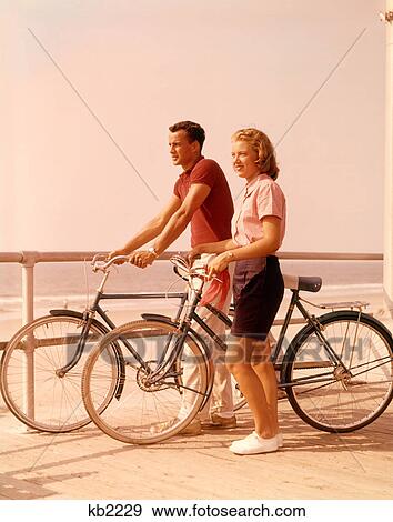 1950S 1960S Teen Couple Standing By Bikes On Beach Boardwalk View Large Photo Image Stock Photo - 1950S 1960S Teen Couple Standing By Bikes On Beach Boardwalk . Fotosearch