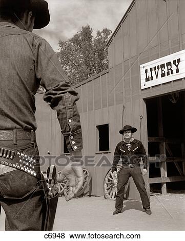 Stock Photo - 1950S 1960S Tv Cowboys In Front Of Livery Stable Ready To Draw Pistols In Gunfight. Fotosearch
