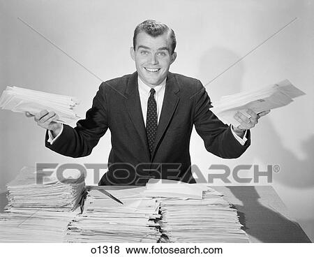 Stock Photo - 1950S Amused Smiling Businessman Holding Papers From The Piles On His Desk. Fotosearch