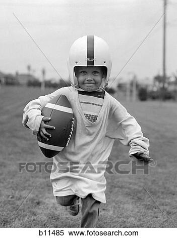 1950S Boy In Oversized Shirt & Helmet Running Toward Camera Holding Football View Large Photo Image Stock Photography - 1950S Boy In Oversized Shirt & Helmet Running Toward Camera Holding Football. Fotosearch