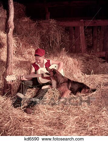 Stock Image - 1950S Boy Playing Guitar Collie Dog Sitting Hay Bales Inside Barn . Fotosearch
