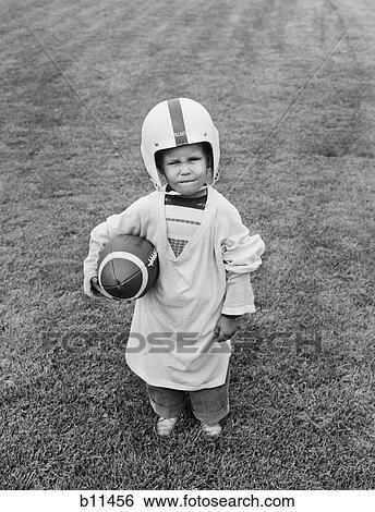 1950S Boy Standing In Grass Wearing Oversized Shirt & Helmet Holding Football View Large Photo Image Stock Photograph - 1950S Boy Standing In Grass Wearing Oversized Shirt & Helmet Holding Football. Fotosearch