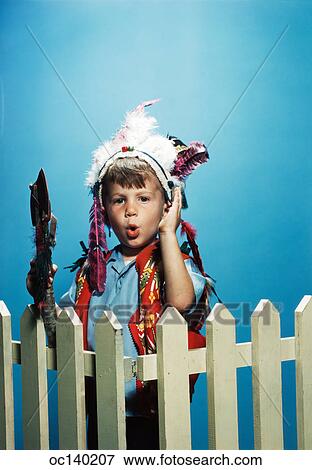 1950S Boy Wearing Native American Indian Feather Headdress Holding Toy Ax Standing Behind Picket Fence Looking At Camera View Large Photo Image Stock Photo - 1950S Boy Wearing Native American Indian Feather Headdress Holding Toy Ax Standing Behind Picket Fence Looking At Camera. Fotosearch