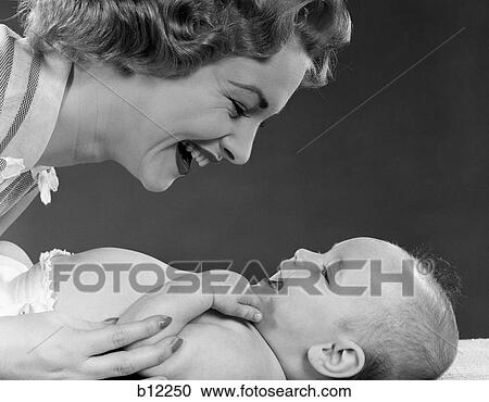 Stock Image - 1950S Close-Up Profile Of Smiling Mother Leaning Toward Laughing Baby Lying On Bed. Fotosearch