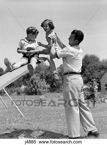 1950S Father Lifting Son And Daughter Onto A Playground Seesaw Outdoor View Large Photo Image Stock Photography - 1950S Father Lifting Son And Daughter Onto A Playground Seesaw Outdoor. Fotosearch
