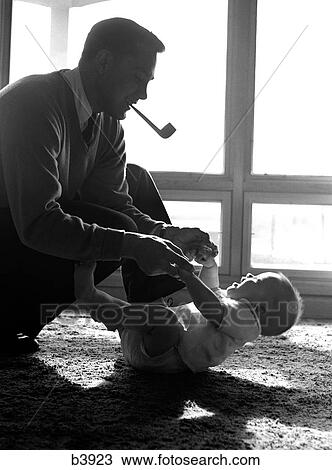 1950S Father Pipe In Mouth Kneeling Down To Play With Baby Laying On Floor Sunlight Coming In Through Windows View Large Photo Image Stock Image - 1950S Father Pipe In Mouth Kneeling Down To Play With Baby Laying On Floor Sunlight Coming In Through Windows. Fotosearch