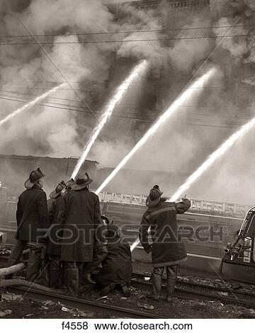 1950S Firemen Using Water Hoses On Smoking Burning Building To Extinguish Fire View Large Photo Image Stock Photo - 1950S Firemen Using Water Hoses On Smoking Burning Building To Extinguish Fire. Fotosearch