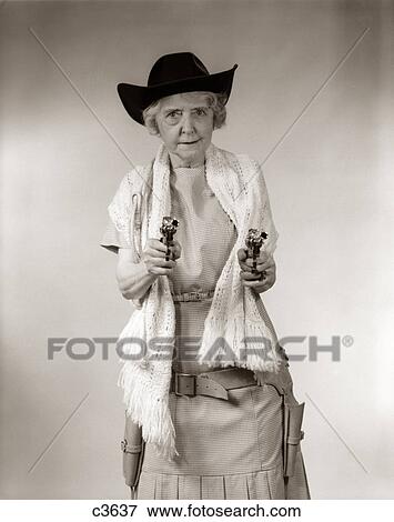 1950S Granny Cowgirl Wearing Hat & Shawl & Pointing 2 Pistols And Looking At Camera View Large Photo Image Stock Photo - 1950S Granny Cowgirl Wearing Hat & Shawl & Pointing 2 Pistols And Looking At Camera. Fotosearch
