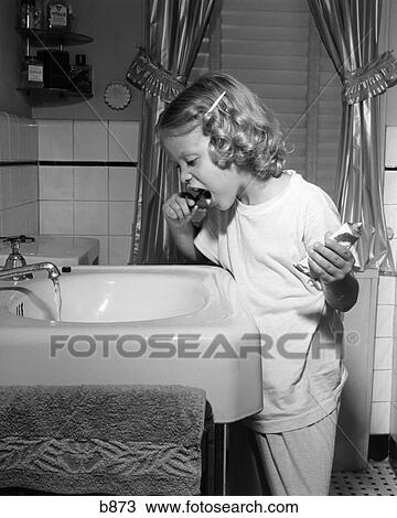 Stock Image - 1950S Little Blond Girl In Pajamas Standing At Bathroom Sink Brushing Her Teeth Toothpaste And Toothbrush In Hand. Fotosearch
