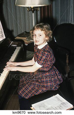 Stock Image - 1950S Little Girl Practicing Playing The Piano Looking At Camera. Fotosearch