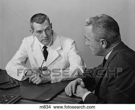 Picture - 1950S Man Doctor Sitting At Desk Talking To Male Patient . Fotosearch