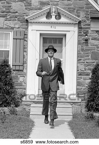 Stock Photo - 1950S Man Smiling Businessman Proud Look Of Satisfaction Walking Out Suburban House Front Door Wearing Hat Carrying Briefcase. Fotosearch