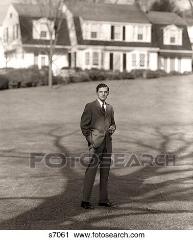 Stock Image - 1950S Man Upscale Businessman Executive In Gray Flannel Suit And Tie Standing On Suburban Home Lawn. Fotosearch