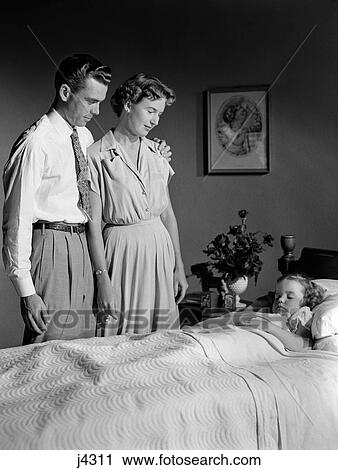 Stock Image - 1950S Mother And Father Watching Sleeping Daughter. Fotosearch
