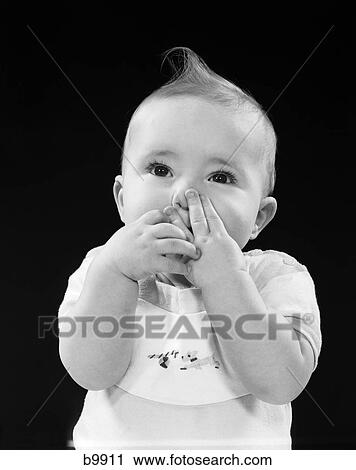 Stock Image - 1950S Portrait Of Baby Covering Mouth With Hands Fingers. Fotosearch