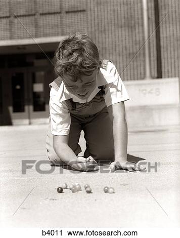 1950S Smiling Boy Ready To Shoot Kneeling On School Yard Ground Playing Game Of Marbles View Large Photo Image Stock Image - 1950S Smiling Boy Ready To Shoot Kneeling On School Yard Ground Playing Game Of Marbles. Fotosearch