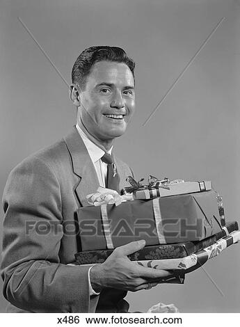Stock Photograph - 1950S Smiling Man Holding Wrapped Christmas Presents Looking At Camera. Fotosearch