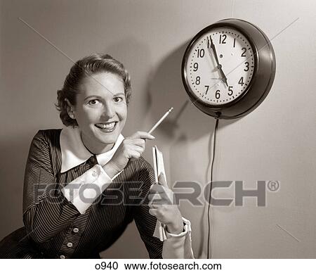 Stock Image - 1950S Smiling Woman Stenographer Office Worker Holding Steno Pad Pointing With Pencil To Clock 5 Minutes Till Quitting Time. Fotosearch