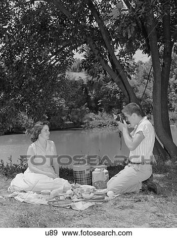 1950S Teenage Couple Picnic Boy Taking Photograph Of Girl Outdoors View Large Photo Image Stock Photo - 1950S Teenage Couple Picnic Boy Taking Photograph Of Girl Outdoors. Fotosearch