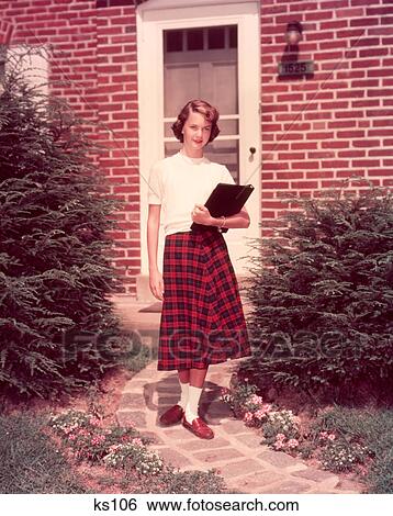 Stock Photograph - 1950S Teenage Girl High School Student Holding School Books Walking Down Flagstone Walk In Front Of Brick House. Fotosearch
