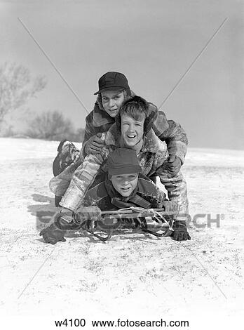 Stock Image - 1950S Three Boys Piled On Top Of Sled On Snow Covered Hill Outdoor Looking At Camera. Fotosearch
