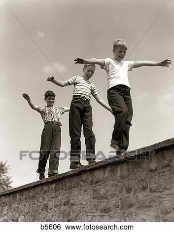1950S Three Laughing Boys Walking On Top Of Stone Wall Arms Out Balancing Playing Follow The Leader View Large Photo Image Stock Photograph - 1950S Three Laughing Boys Walking On Top Of Stone Wall Arms Out Balancing Playing Follow The Leader. Fotosearch