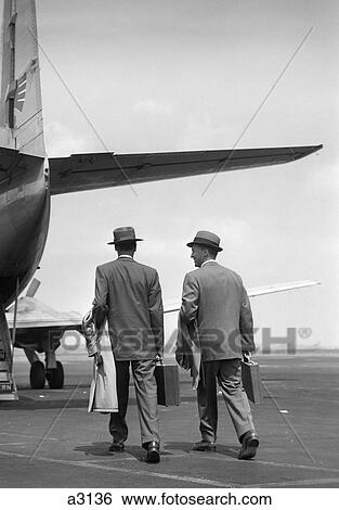 1950S Two Men Businessmen Wearing Hats Carrying Overcoats And Briefcases Walking Together To Board Propeller Airliner View Large Photo Image Stock Photograph - 1950S Two Men Businessmen Wearing Hats Carrying Overcoats And Briefcases Walking Together To Board Propeller Airliner. Fotosearch