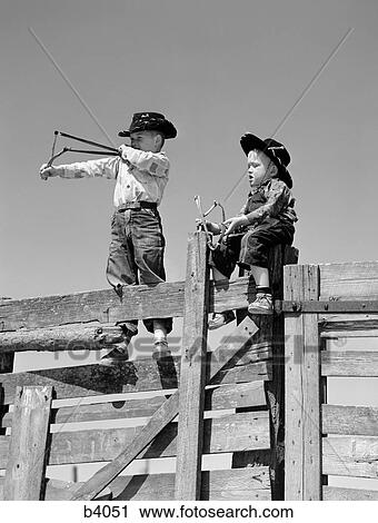 1950S Two Young Boys Dressed As Cowboys Shooting Slingshots On Top Of Wooden Fence Outdoor View Large Photo Image Stock Image - 1950S Two Young Boys Dressed As Cowboys Shooting Slingshots On Top Of Wooden Fence Outdoor. Fotosearch