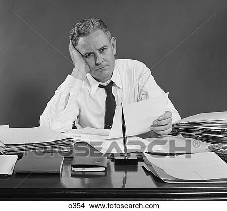 1950S Unhappy Overworked Businessman Sitting At Desk Holding Papers View Large Photo Image Picture - 1950S Unhappy Overworked Businessman Sitting At Desk Holding Papers . Fotosearch