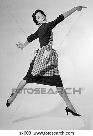 Stock Photo - 1950S Woman Housewife In Gingham Apron Running And Jumping Into Air Smiling And Pointing Index Finger Studio High Heel Shoes. Fotosearch