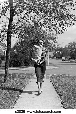 1950S Woman Walking On Sidewalk Carrying A Grocery Bag Full Of Food View Large Photo Image Stock Photograph - 1950S Woman Walking On Sidewalk Carrying A Grocery Bag Full Of Food. Fotosearch