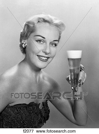Stock Photo - 1950S Woman Wearing Strapless Evening Gown Holding Up Tall Pilsner Glass Of Beer Looking At Camera. Fotosearch
