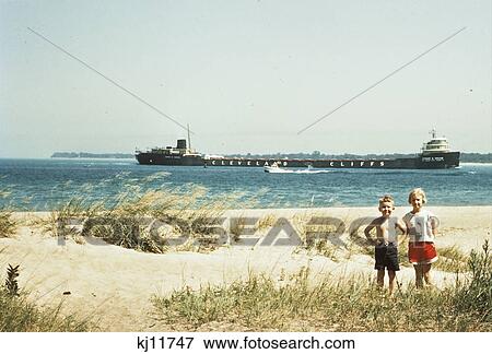 1950S Young Boy And Girl On Beach Smiling With A Tanker Ship On Lake Behind Them Port Huron Michigan 1955 View Large Photo Image Stock Photo - 1950S Young Boy And Girl On Beach Smiling With A Tanker Ship On Lake Behind Them Port Huron Michigan 1955. Fotosearch
