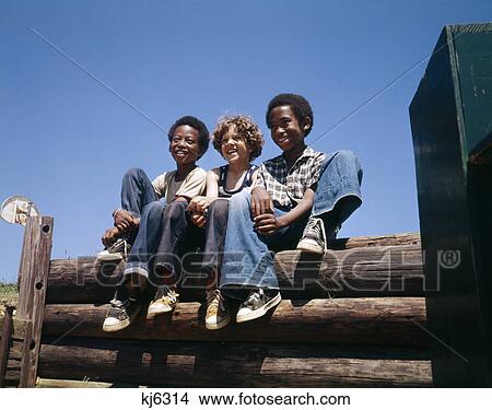 1960S 1970S 3 Boys Sitting Log Fence Smiling Wearing Blue Jeans 2 African American 1 Caucasian View Large Photo Image Picture - 1960S 1970S 3 Boys Sitting Log Fence Smiling Wearing Blue Jeans 2 African American 1 Caucasian . Fotosearch