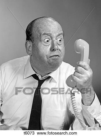 Stock Image - 1960S 1970S Angry Balding Man Looking Bug-Eyed Into Telephone Receiver. Fotosearch
