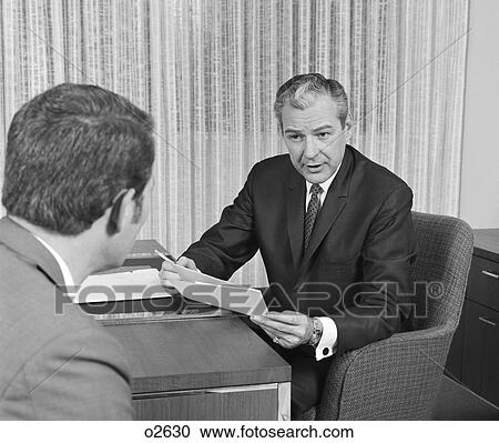 1960S 1970S Man From Behind Meeting At Desk Of Older Businessman View Large Photo Image Stock Image - 1960S 1970S Man From Behind Meeting At Desk Of Older Businessman . Fotosearch