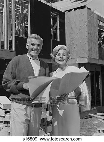 Stock Photo - 1960S 1970S Smiling Mature Couple Holding Blueprints On Home Construction Site. Fotosearch