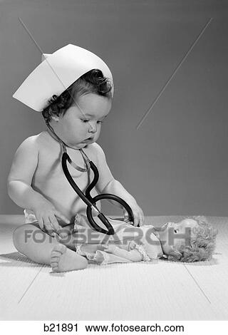 Stock Image - 1960S Baby Playing Nurse With Hat Doll And Stethoscope. Fotosearch