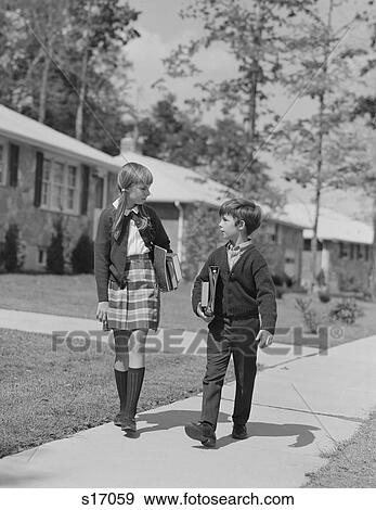 Stock Photo - 1960S Boy Girl Carrying Books Walking To School In Suburban Neighborhood. Fotosearch