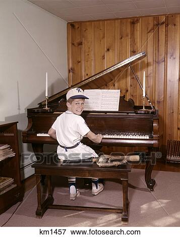 Stock Photo - 1960S Boy Playing Piano Wearing Baseball Uniform Looking At Camera. Fotosearch