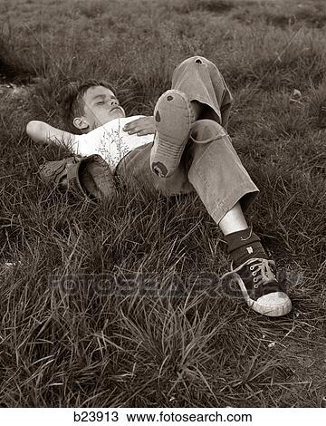 Stock Image - 1960S Boy Sleeping In Grass Legs Crossed Holes In Sneakers Baseball Mitt By His Side. Fotosearch