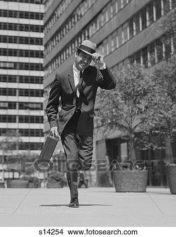 1960S Businessman Carrying Briefcase Holding His Hat On Running Down Urban Sidewalk View Large Photo Image Picture - 1960S Businessman Carrying Briefcase Holding His Hat On Running Down Urban Sidewalk. Fotosearch