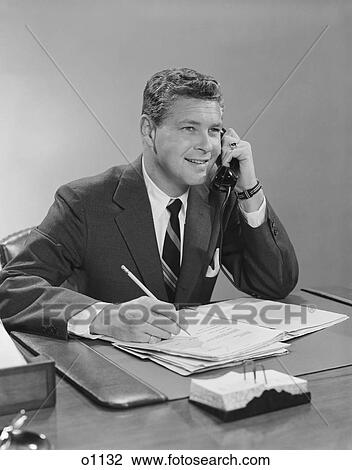 1960S Businessman Seated At Desk Talking On Telephone Smiling Writing With Pencil View Large Photo Image Stock Image - 1960S Businessman Seated At Desk Talking On Telephone Smiling Writing With Pencil. Fotosearch
