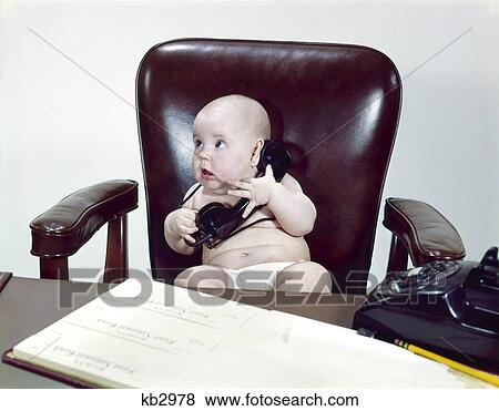 Stock Photo - 1960S Chubby Baby Sitting In Leather Chair At Office Desk Holding Telephone. Fotosearch