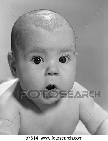 Picture - 1960S Close-Up Of Baby Lying On Stomach Wide-Eyed With Mouth Open Looking At Camera. Fotosearch