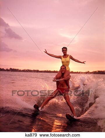 1960S Couple Water Skiing Woman Yellow Bathing Suit Riding On The Shoulders Of Man Red Trunks At Sunset View Large Photo Image Stock Photo - 1960S Couple Water Skiing Woman Yellow Bathing Suit Riding On The Shoulders Of Man Red Trunks At Sunset . Fotosearch